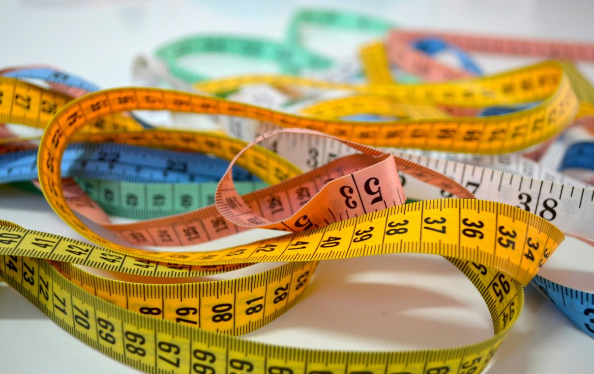 Colorful measuring tapes snake across a flat surface, overlapping and looping in a loose pile on a white tabletop.