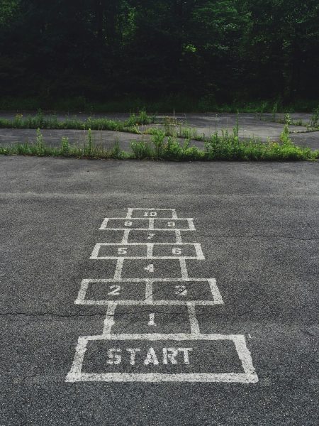 Painted hopscotch grid on cracked asphalt leading toward overgrown weeds and trees, numbered ascending toward the far edge. Text: START; 1, 2, 3, 4, 5, 6, 7, 8, 9, 10.